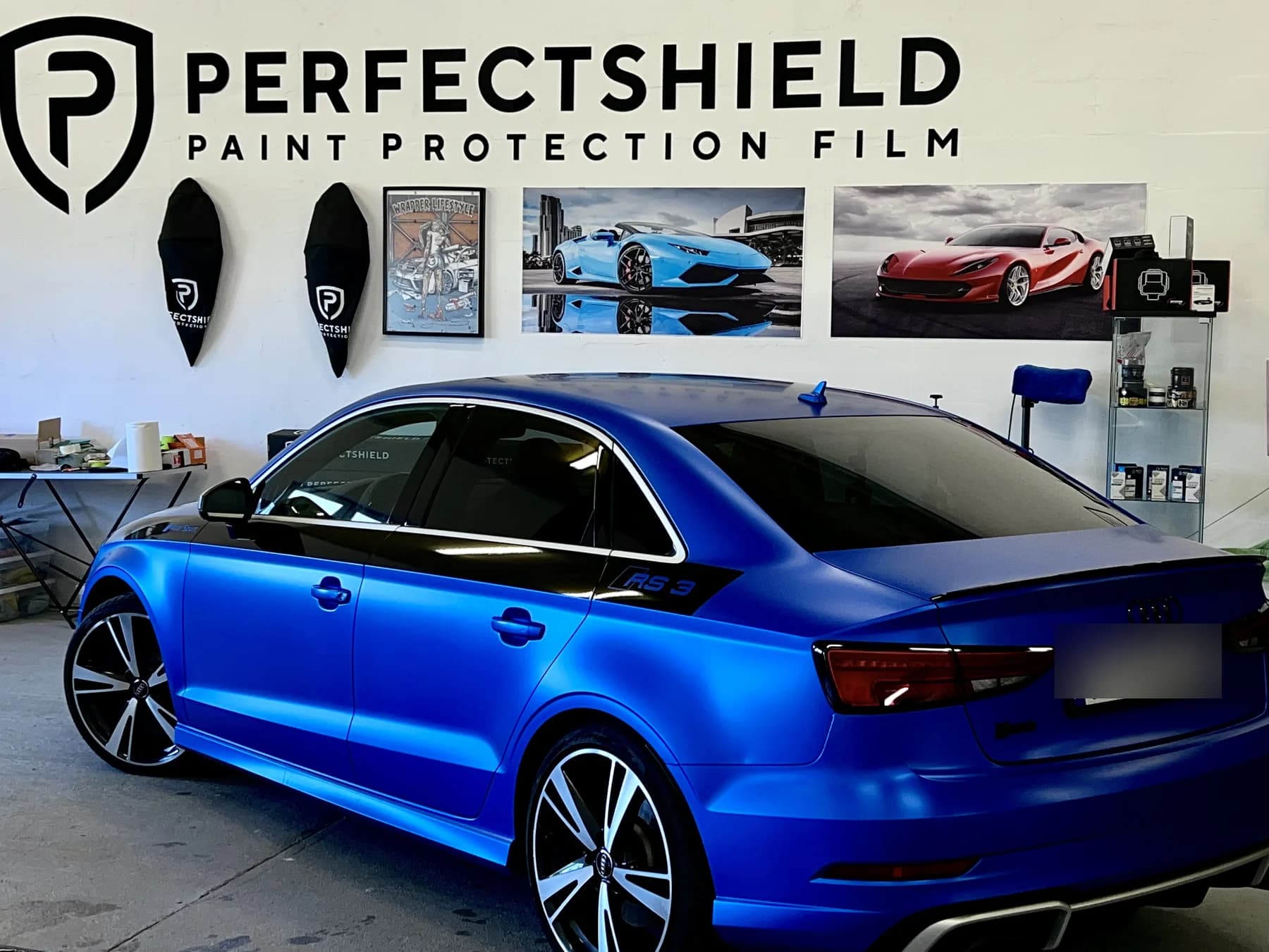 Audi RS3 w wersji limuzyna pokryte satynową niebieską folią, sfotografowane z boku w hali studia.