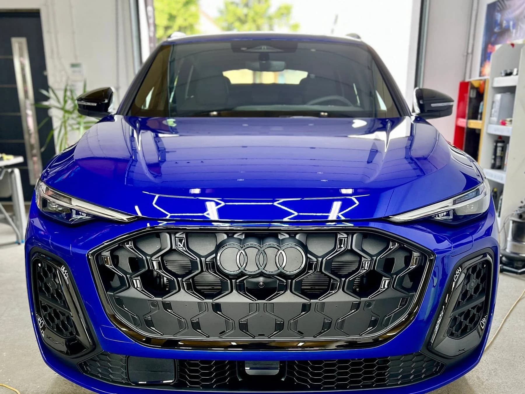 Przód niebieskiego SUV-a Audi z atrapą typu plaster miodu, auto w hali studia po zabezpieczeniu folią ochronną.
