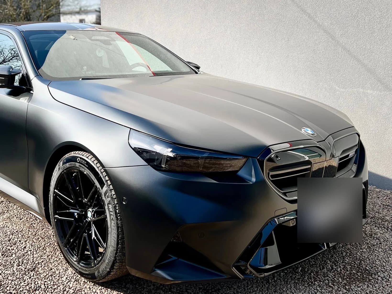 BMW M5 w satynowej szarości pod skosem z przodu, z czarnymi felgami — auto stoi na podjeździe przed studiem.