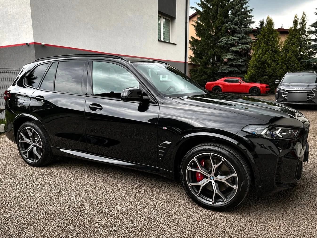 Czarne BMW X5 pod skosem z przodu na podjeździe studia — lakier po detailingu odbija otoczenie.