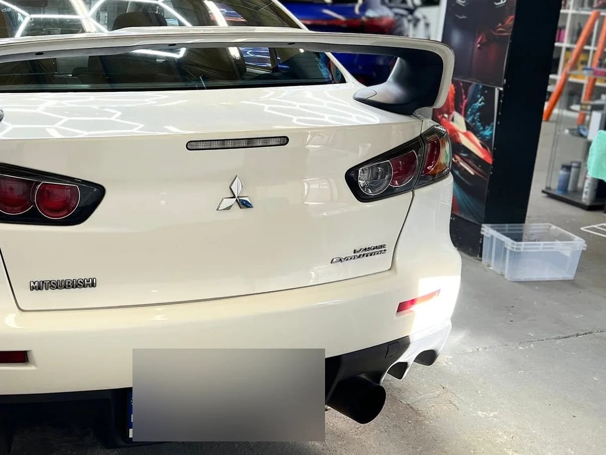 Tył białego Lancera Evolution X ze spojlerem, auto stoi w hali studia po detailingu.