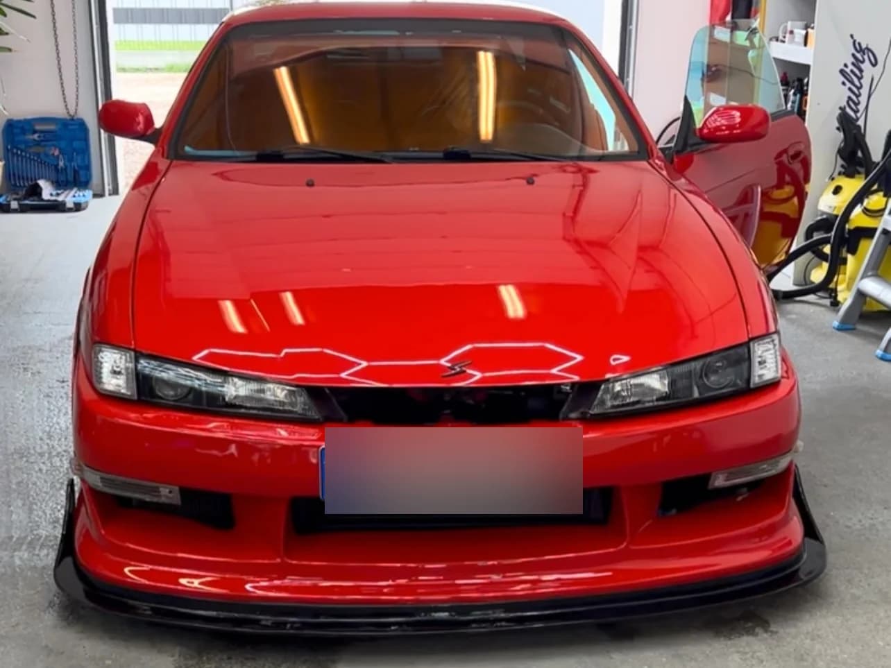 Czerwony Nissan Silvia S14 w otwartej bramie studia, ujęcie z przodu — auto po detailingu, z niskim splitterem.