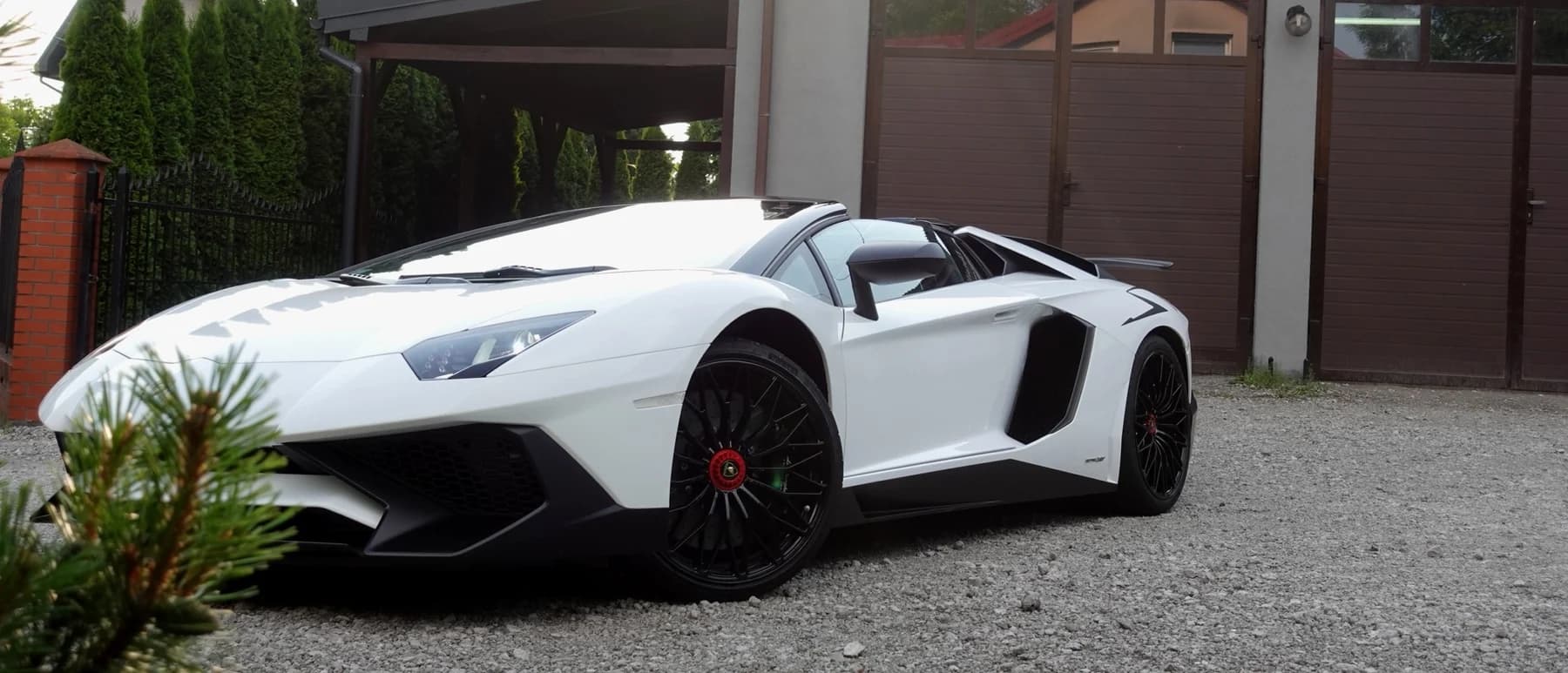 Białe Lamborghini Aventador SV Roadster przed budynkiem studia Auto Estetyka w popołudniowym słońcu.