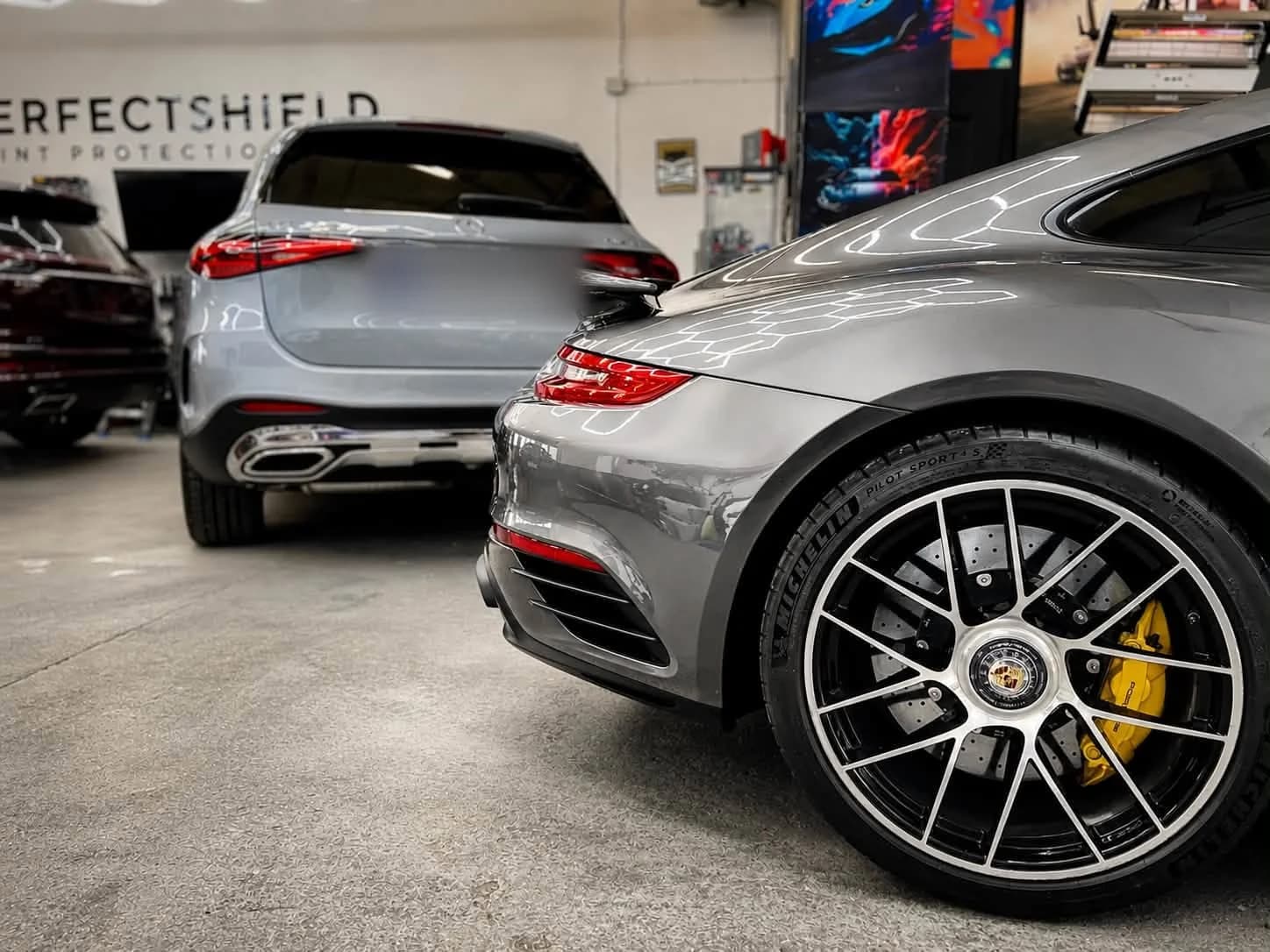 Porsche 911 Turbo S i Mercedes GLC w hali studia, na ścianie baner PerfectShield Paint Protection
