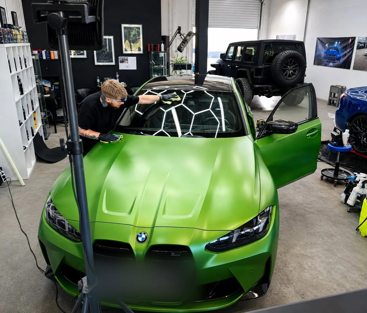 Detailer pracuje przy limonkowo-zielonym BMW M4 w trakcie oklejania — na masce odbijają się plastry lamp studia.