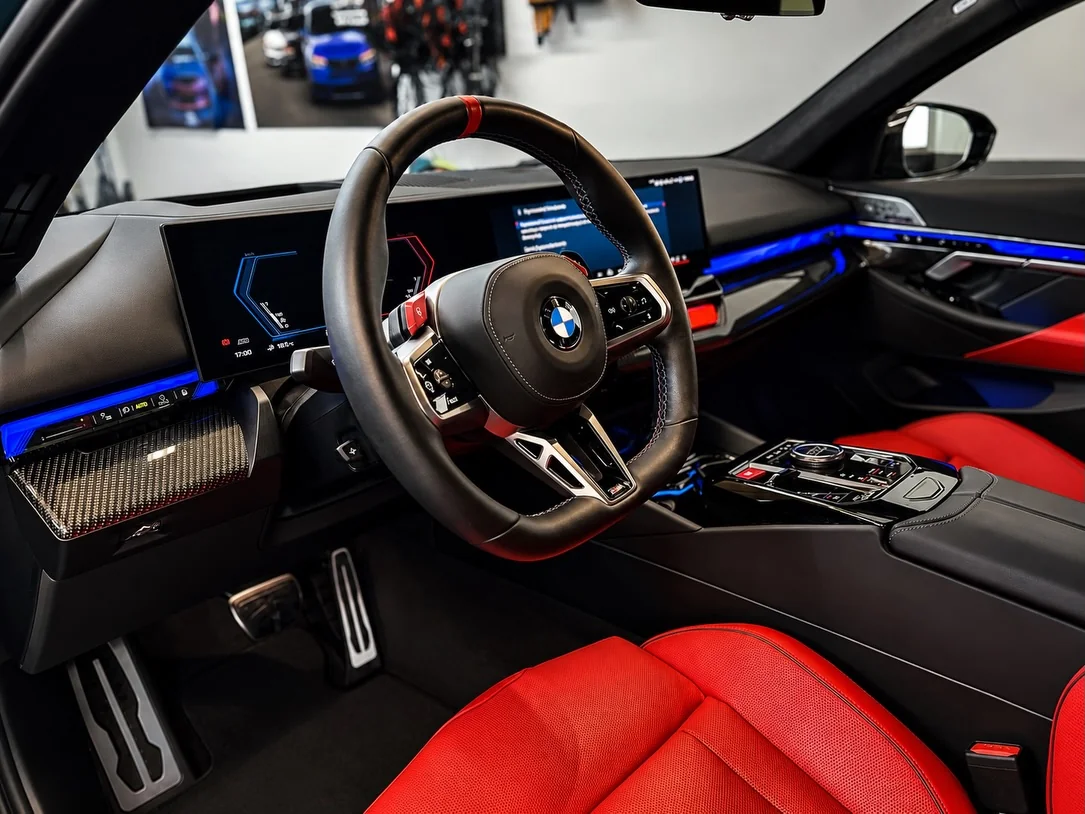 Kokpit zielonego BMW M5 po czyszczeniu wnętrza — kierownica M, zakrzywiony ekran i niebieskie podświetlenie ambiente.