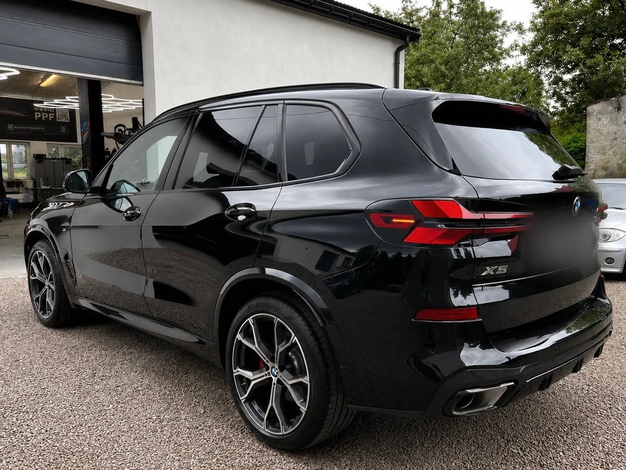 Czarne BMW X5 pod skosem od tyłu po detailingu nadwozia, auto stoi przed halą studia.