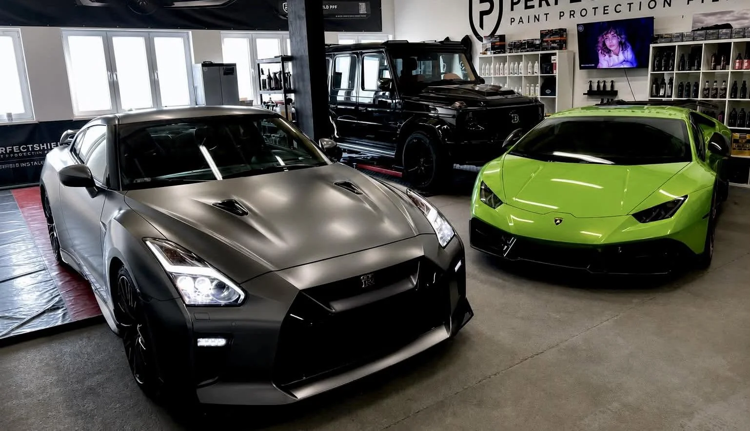 Hala studia Auto Estetyka z trzema autami: matowo-szary Nissan GT-R, limonkowe Lamborghini Huracán i czarny Mercedes klasy G.