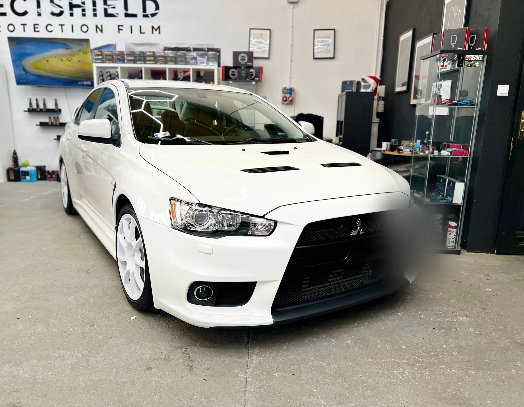 Białe Mitsubishi Lancer Evolution X w hali studia Auto Estetyka, ujęcie z przodu pod skosem po detailingu.