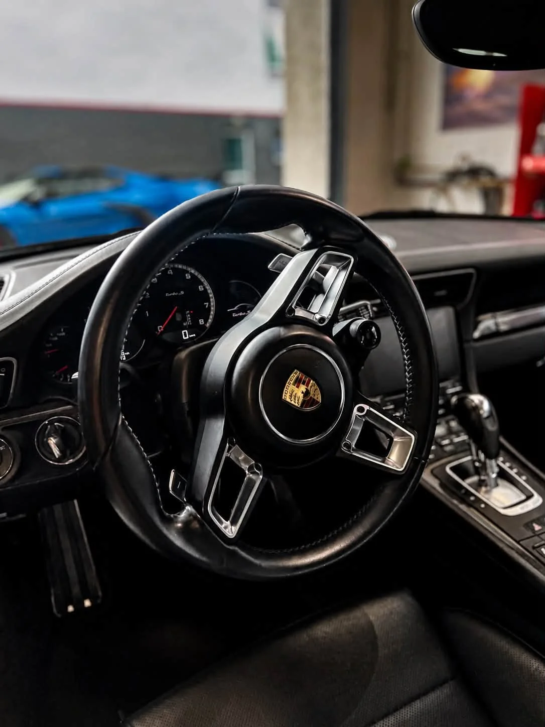 Kierownica Porsche 911 Turbo S z herbem marki po czyszczeniu wnętrza, w tle zegary i deska rozdzielcza.