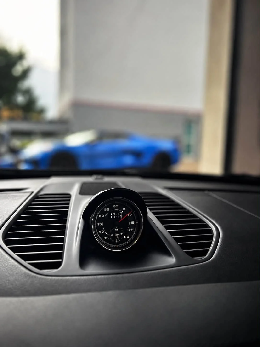Zegar analogowy na desce rozdzielczej Porsche 911 po czyszczeniu detailingowym, w tle rozmyta hala studia.