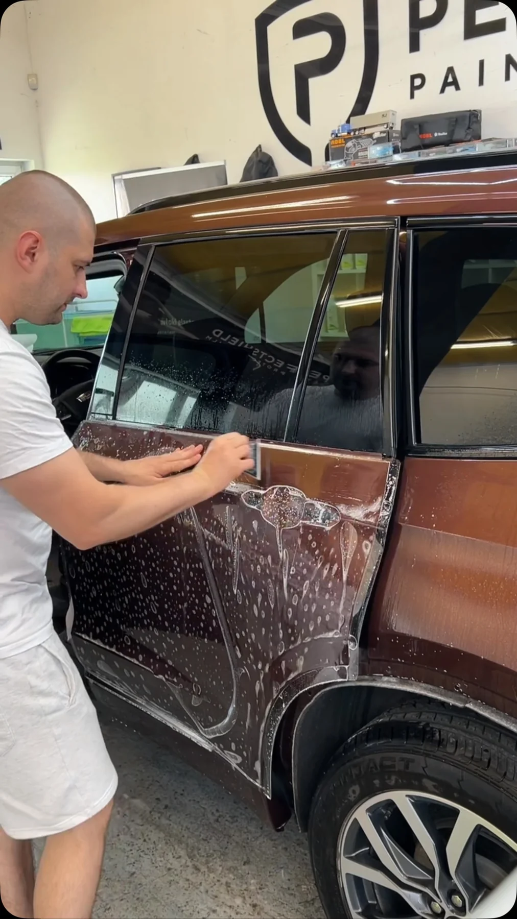Detailer naciąga folię ochronną PPF na drzwiach miedzianego SUV-a metodą mokrą, wygładzając ją do krawędzi.
